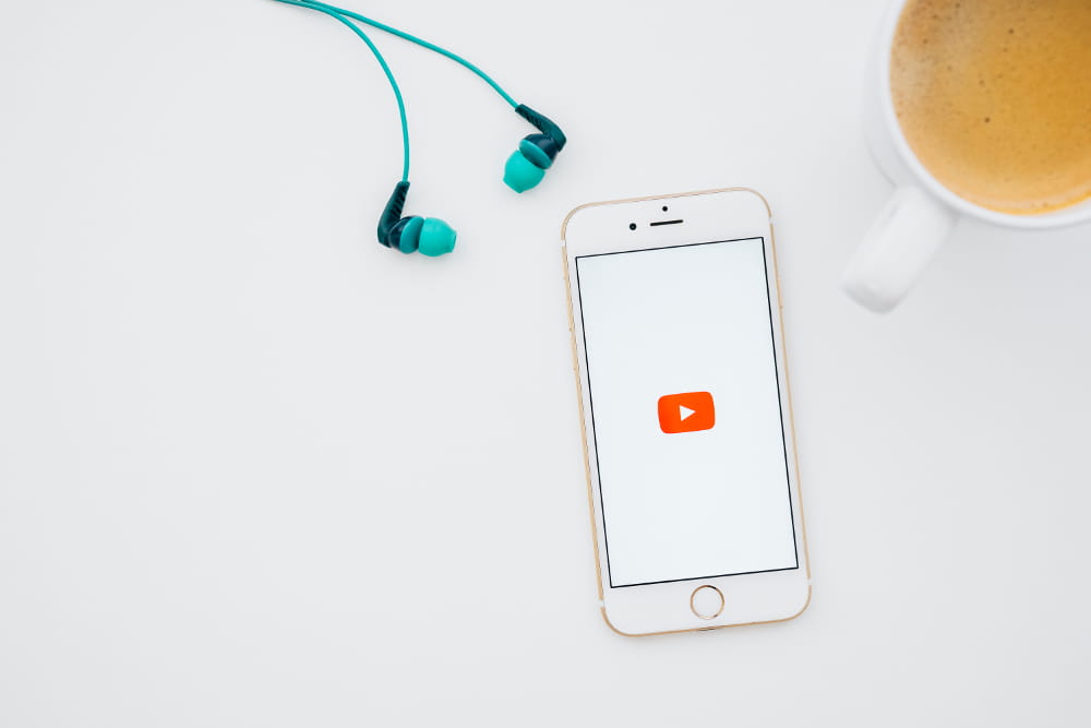 Como fazer marketing digital no YouTube: celular acessando YouTube, fone de ouvido e uma xícara de café.