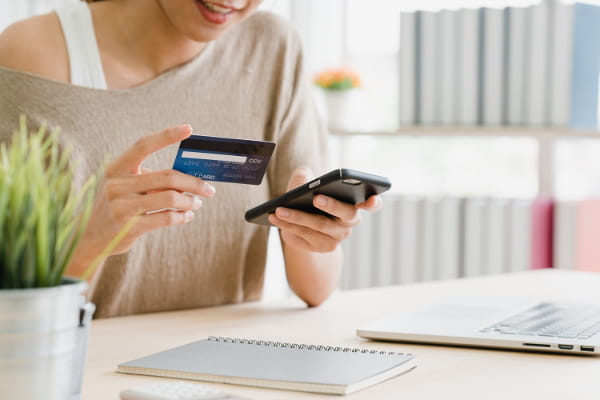 Jornada de compra do cliente: mulher segurando seu cartão de crédito em uma mão e o celular em outra.