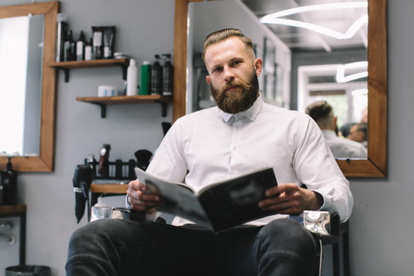 Criação de Sites para Barbearia: Barbeiro sentado na cadeira lendo uma revista.