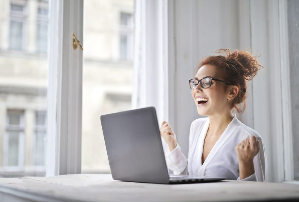 Dicas para fazer a criação de seu site: mulher feliz acessando site pelo notebook.