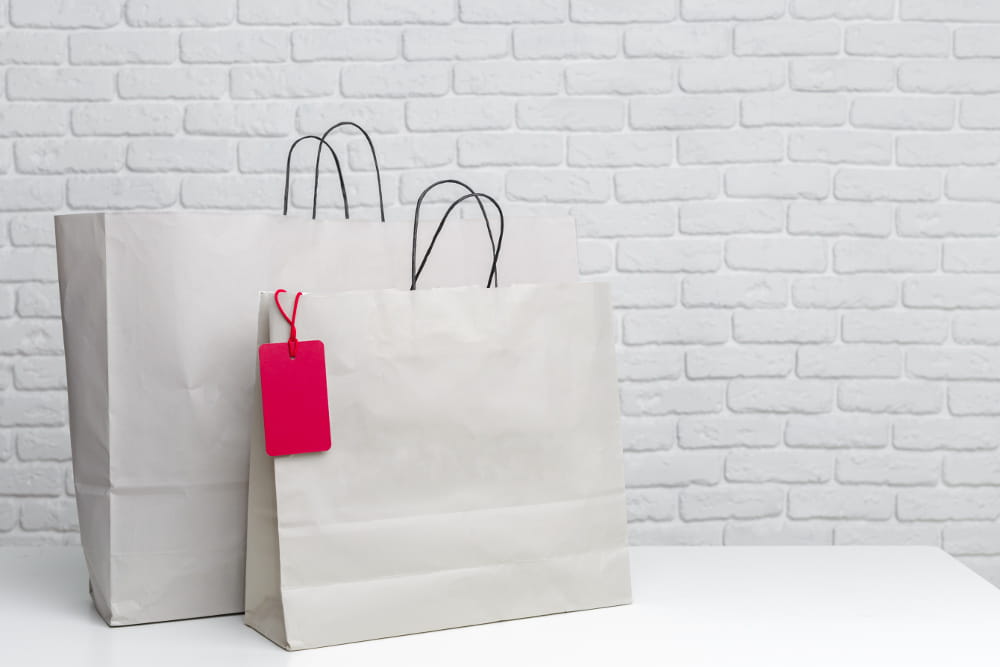 Jornada de compra do cliente: duas sacolas de compras com parede de tijolos cinza ao fundo.