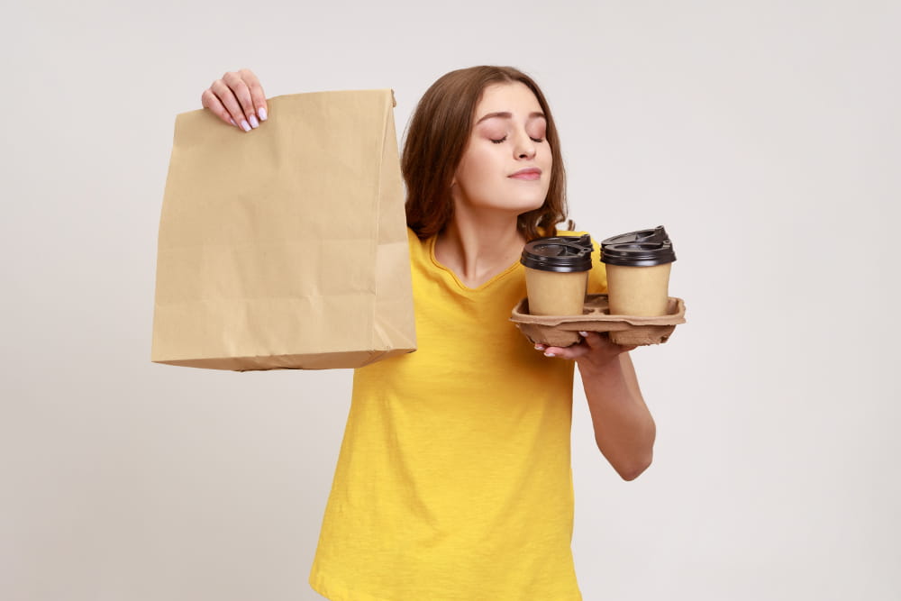 Marketing sensorial: o que é e como aplicar: mulher segurando cafés e um pacote com comida.